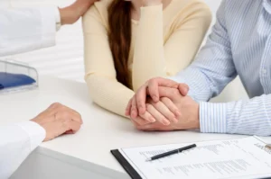A young couple sitting in a bright TCM clinic in Singapore, consulting with a traditional Chinese medicine practitioner about holistic infertility support.