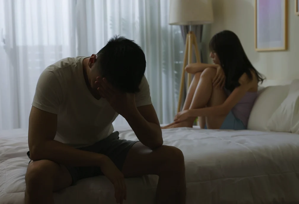 Distressed couple sitting apart on a bed coping with emotional distress after ivf failure singapore.