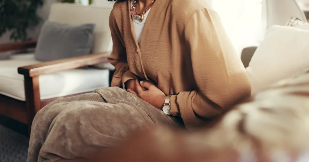 Woman sitting on a sofa holding her abdomen due to pelvic pain linked to ovarian cyst and fertility Singapore concerns.