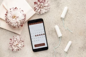 Smartphone showing period tracking calendar alongside tampons and flowers representing signs of low AMH.